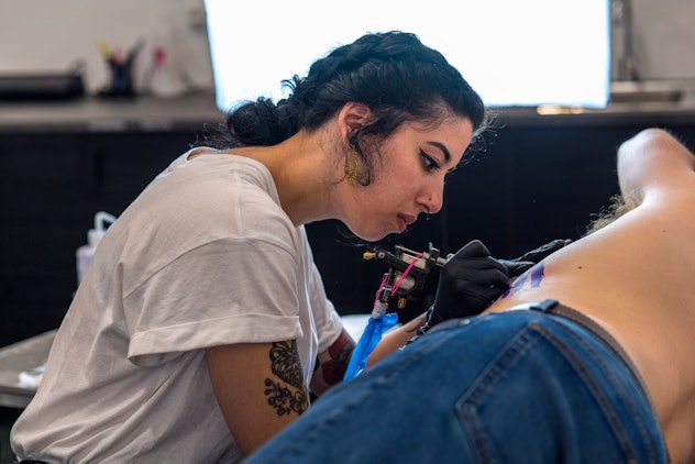 Young woman tattooing on the ribs. She is brunette with tattoo machine. She is very concentrated.
