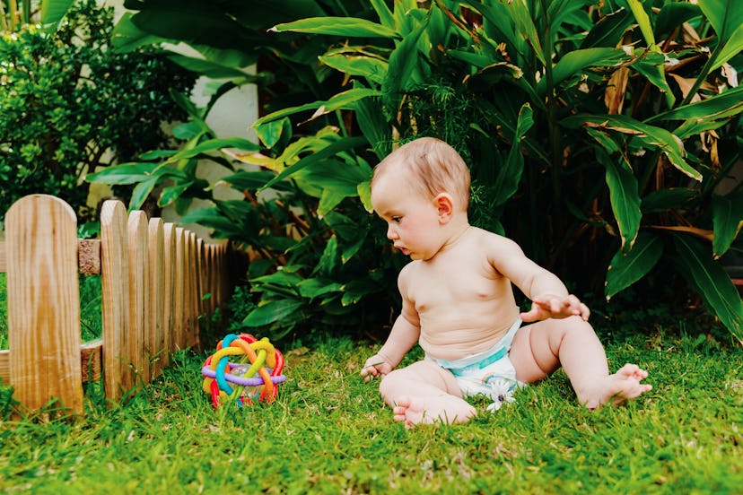 Baby sitting on the barefoot lawn playing with a colorful toy to stimulate his senses.