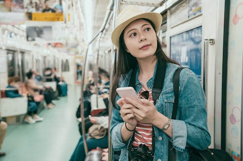 Young asian woman backpacker using smartphone in subway train. girl traveler smiling holding mobile ...