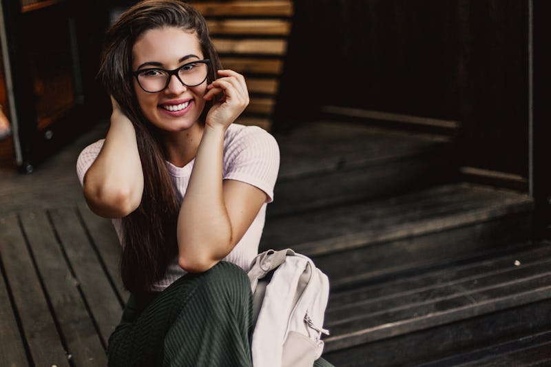 Happy smiling woman in glasses sitting on wooden steps in street.