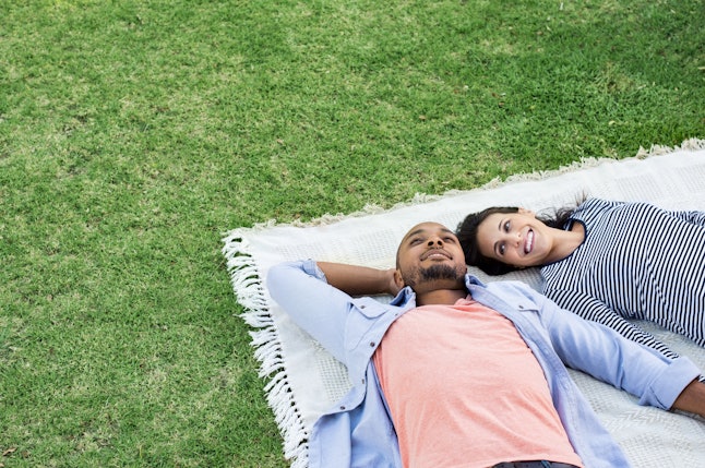 Young multiethnic couple lying on blanket on grass. Latin woman with her african boyfriend relaxing on picnic blanket outdoor. Mature happy couple in love lying on grass with copy space.