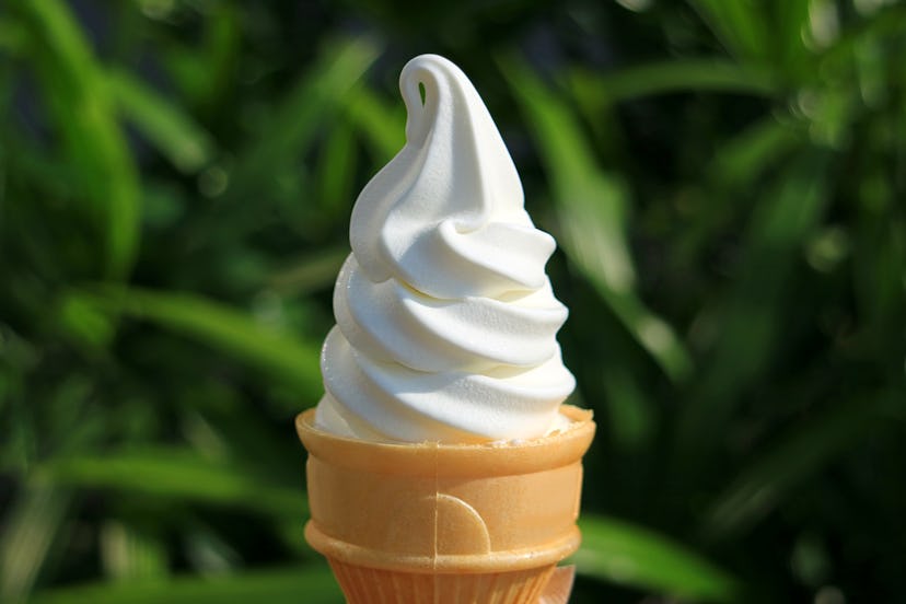 Pure White Vanilla Soft Serve Ice Cream Cone, Blurred Green Foliage in Background 
