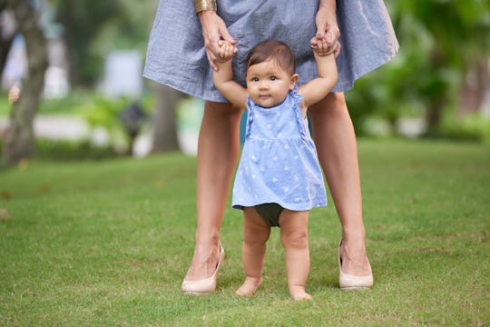 Adorable little girl making first steps with help of her mother