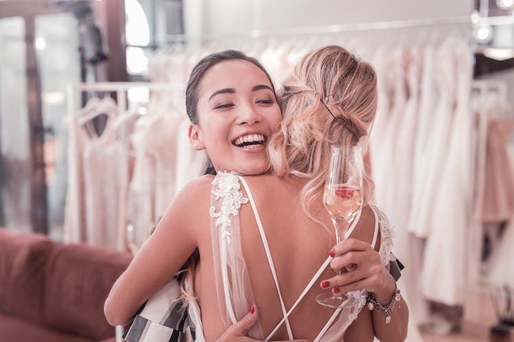 Wedding celebration. Joyful pleasant woman holding a glass with champagne while hugging her best fri...