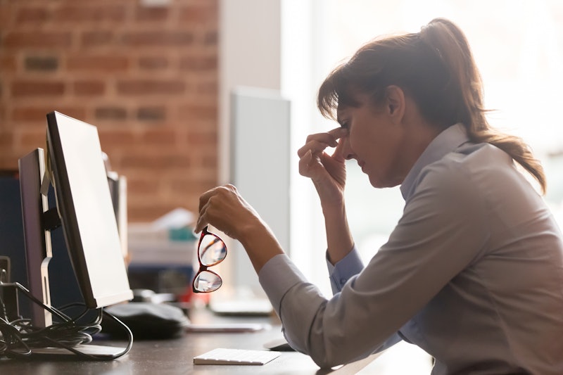 Stressed overworked middle aged businesswoman office worker taking off glasses tired from computer w...