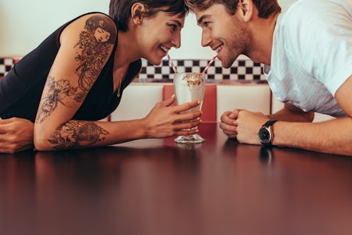 Close up of happy couple sharing a milk shake with straws sitting opposite to each other at a restau...