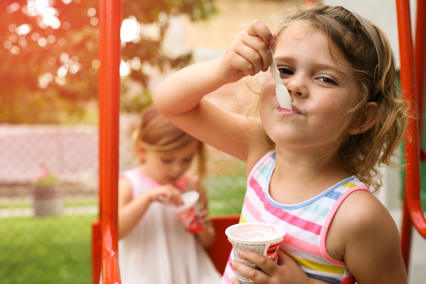 Cute little girl eating ice cream outside. Focus is on girl on foreground.  