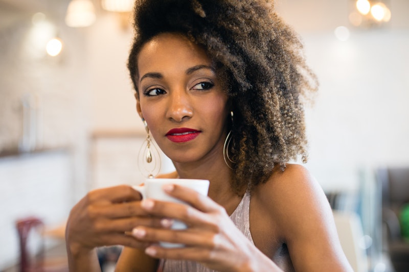 Stylish pensive black woman drinking a coffee in a cafe bar.