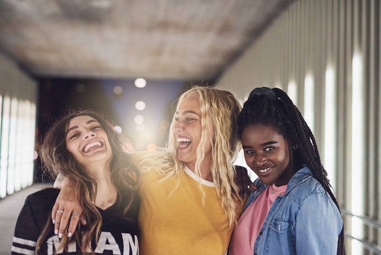 Laughing group of diverse young girlfriends having fun while walking together down a walkway in the ...