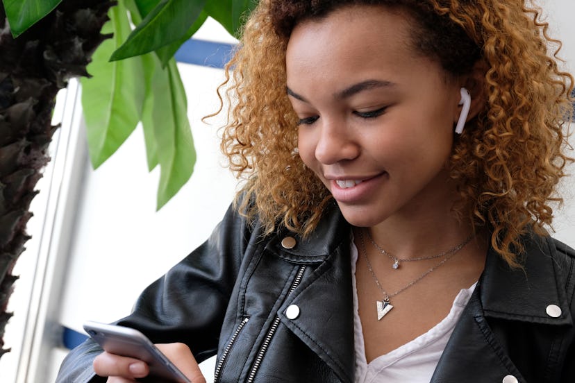 A beautiful young modern black woman, in a leather jacket with airpods in her ear, listens to music....