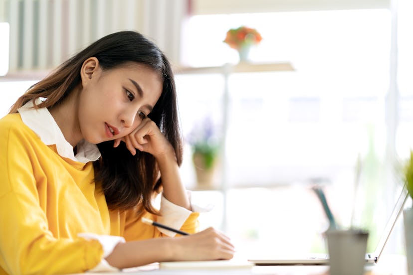 Young attractive asian female student sitting at table thinking and writing journal by hand note ide...