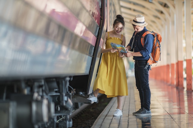 Couples travellers, read the map to plan travel on the platform in railway station.