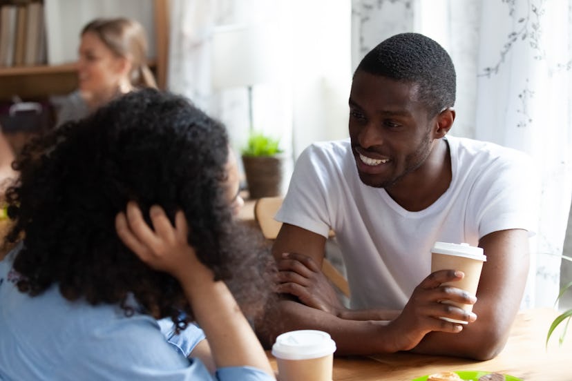 Rear view of mixed race female chatting with african american friend sitting together in cafe drinki...