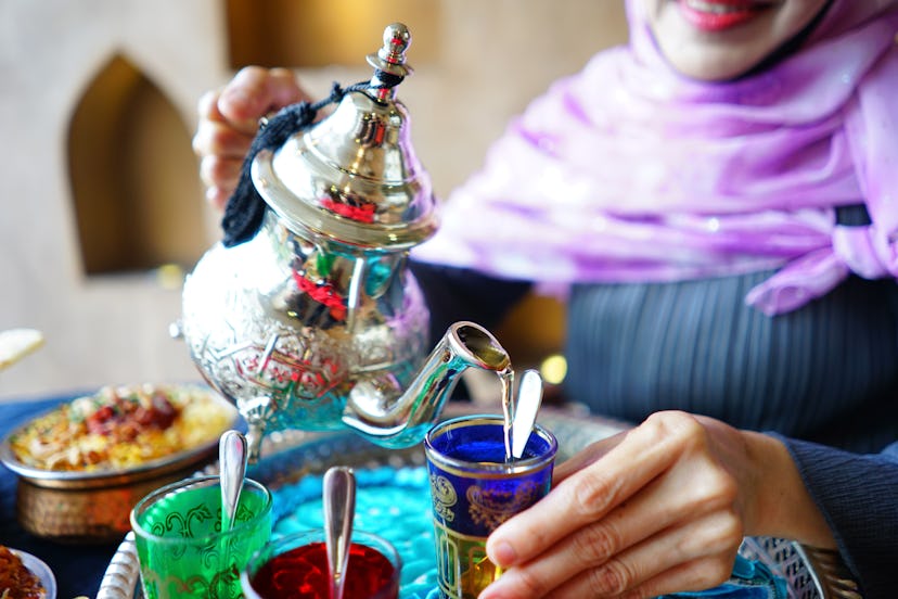 Female hand pouring Moroccan mint tea from traditional tea pot into a glass with blurred Chicken Bir...
