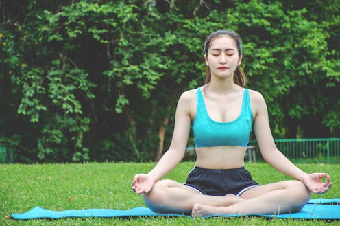 Woman meditating in a lotus yoga position on a yoga mat in the park