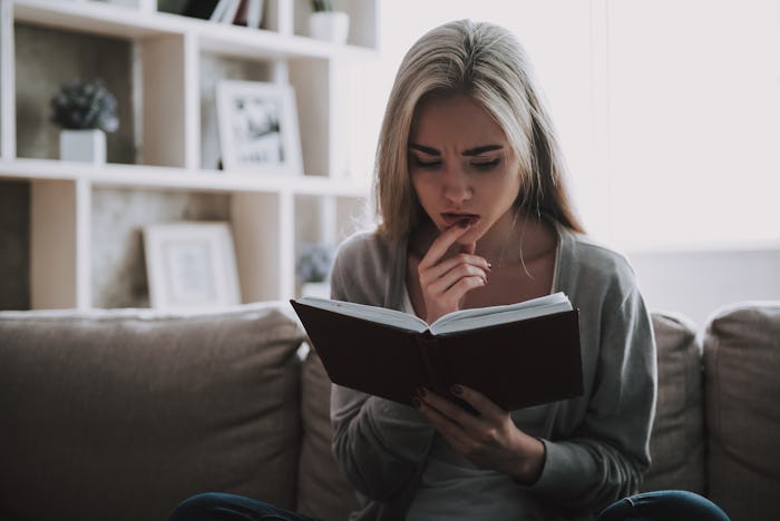 Young Beautiful Woman Reading Book at Home. Portrait of Attractive Thoughtful Girl Sitting on Sofa a...