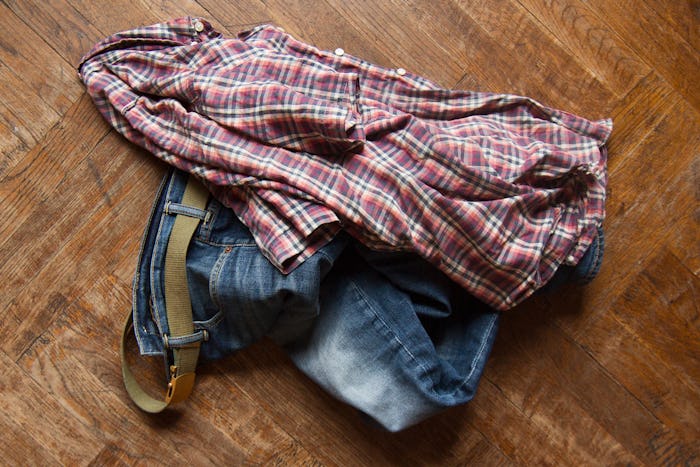 top view of man blue jeans and squared shirt thrown on the wooden floor 
