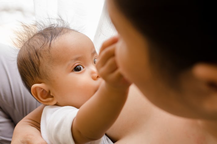 Mother breastfeeding her newborn baby beside window. Milk from mom’s breast is a natural medicine fo...