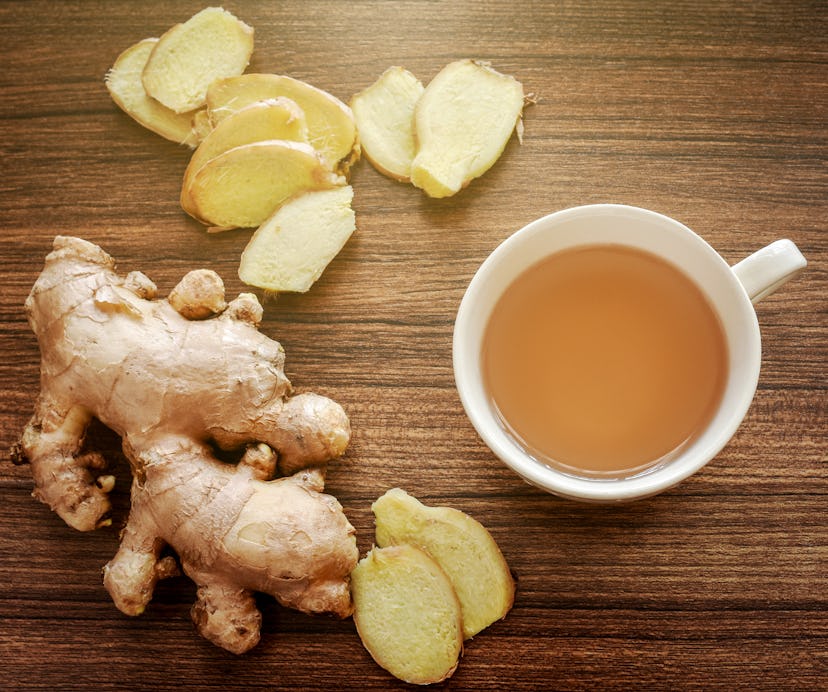 Ginger root and slices on wood background with a cup of ginger tea. Ginger tea helps warming the bod...