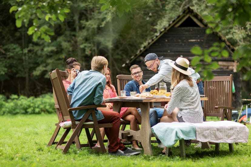 leisure, holidays, eating, people and food concept - happy friends having dinner at summer garden pa...