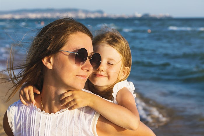 Happy mom and daughter smile at each other while walking near the sea on a warm sunny evening