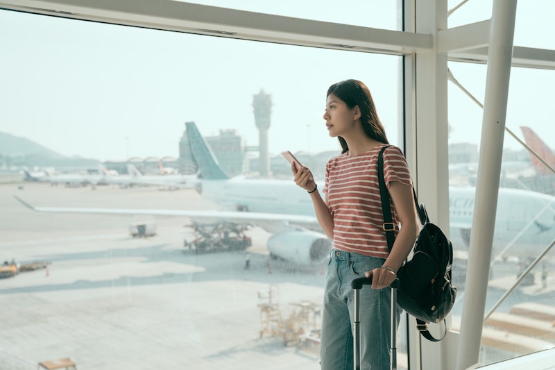Young asian woman backpacker in airport waiting for airplane. japanese female holding mobile phone s...