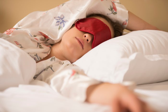 Tired woman sleeping in bed wearing blindfold sleep mask. Young girl taking nap.