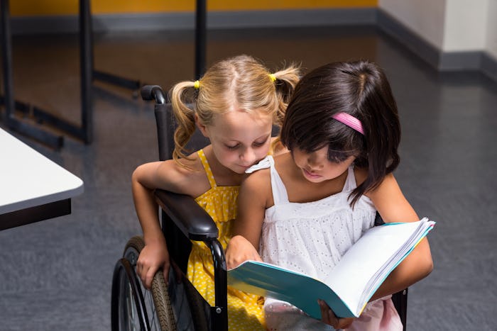 Cute girls sitting on wheelchair reading book in class room