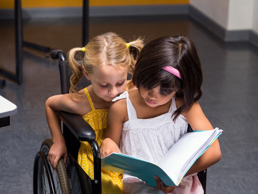 Cute girls sitting on wheelchair reading book in class room