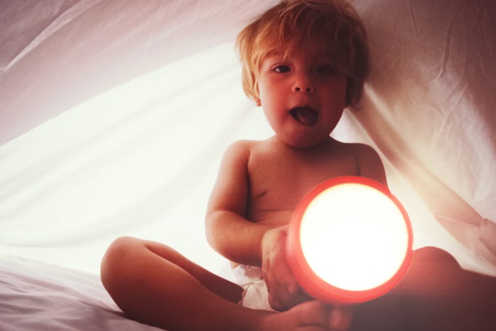 Toddler boy in diaper with flashlight under the sheets, filtered toned snapshot image with noise add...