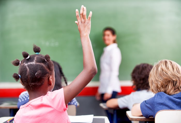 Happy schoolchildren at primary school raising hand in elementary multi ethnic classroom.