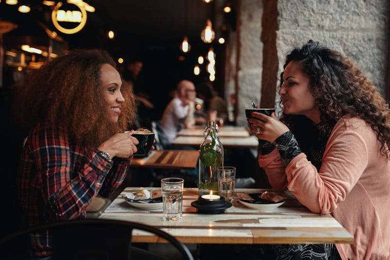 Side view portrait of two young women talking and drinking coffee in a cafe. Female friends in a res...