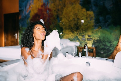 Cheerful black young woman relaxed in the hydro massage bath playing and covered in foam