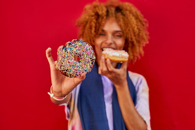  Curly Hair woman eating a donut on a red wall and showing the other one to the camera.             ...