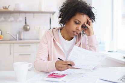 Upset african american female sitting at kitchen table with laptop, dealing with financial stress an...