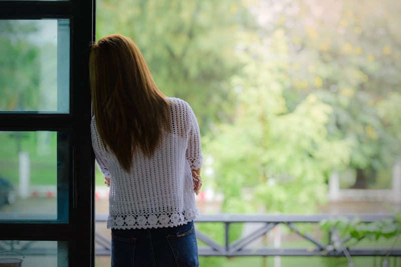 A woman with long hair looks out at a green treescape. Experts explain signs you might be repressing...