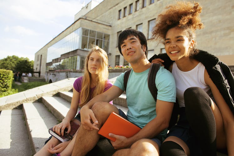 cute group of teenages at the building of university with books huggings, smiling, back to school
