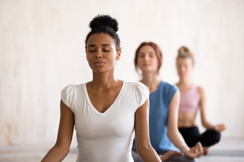 Group diverse young beautiful women sitting in lotus position meditating during session at yoga stud...