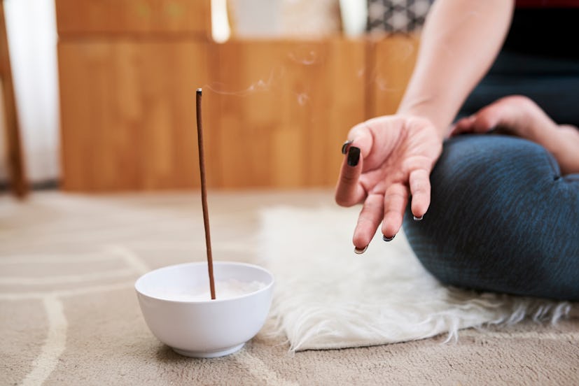 Bowl with scented aroma stick next to meditating young woman