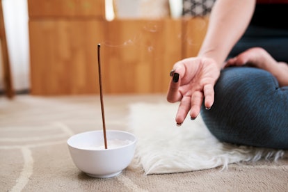 Bowl with scented aroma stick next to meditating young woman