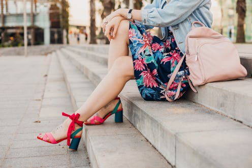 close up details of legs in pink sandals of woman sitting on stairs in city street in stylish printe...