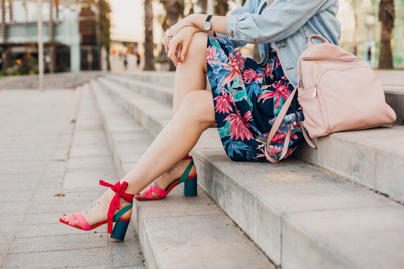 close up details of legs in pink sandals of woman sitting on stairs in city street in stylish printe...