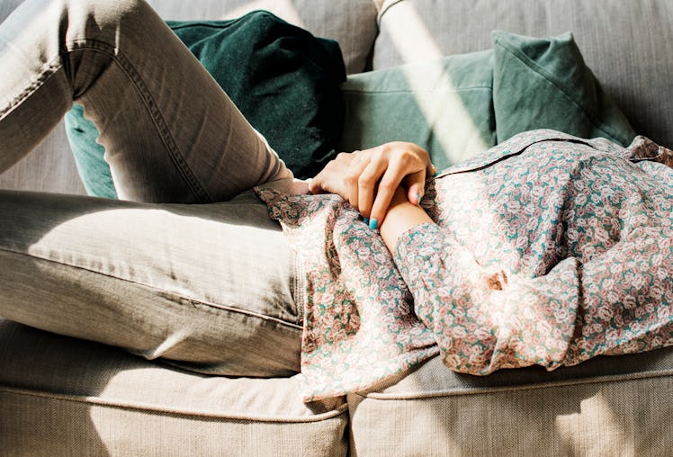 A woman with grey jeans and a printed top lies on her couch and rests in the sunlight.