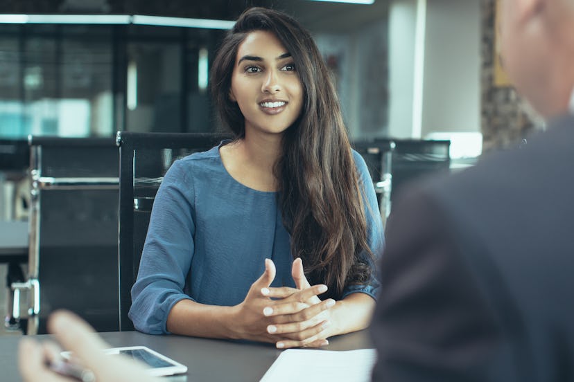 Portrait of young Indian female client or candidate sitting at table, talking to senior male manager...