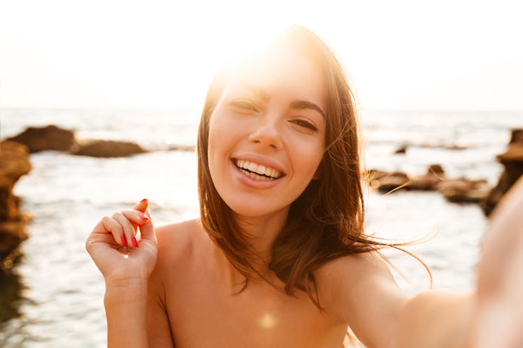 Close up image of happy brunette woman making selfie on beach