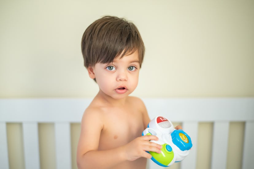 Cute baby boy toddler - in the crib holding toy camera