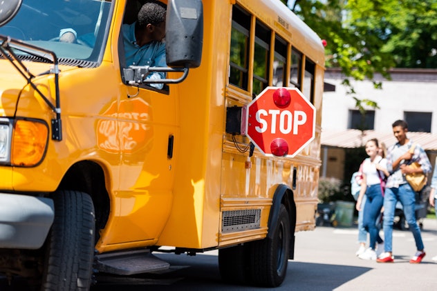 senior school bus driver looking at teens walking behind bus