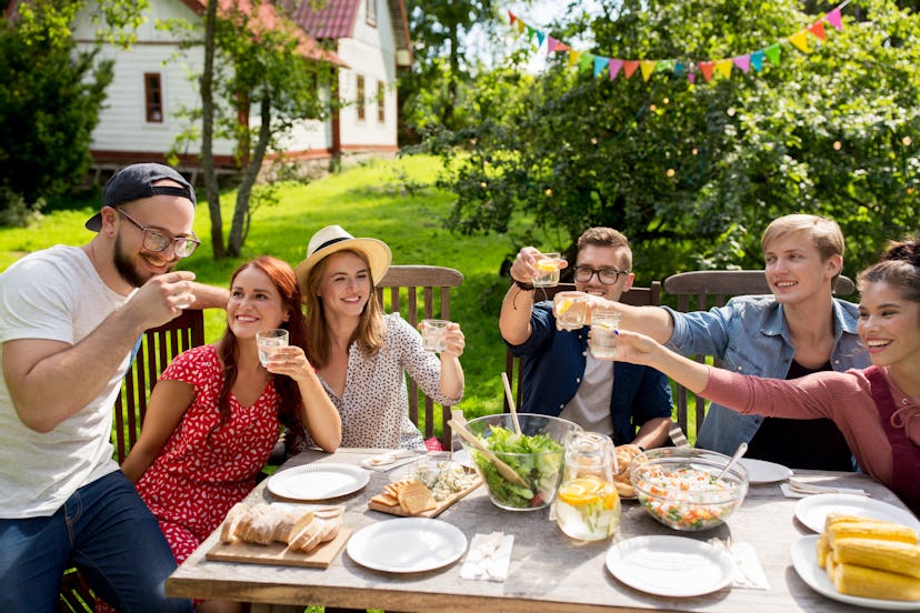 summer, holidays, celebration people and food concept - happy friends having garden party and clinki...