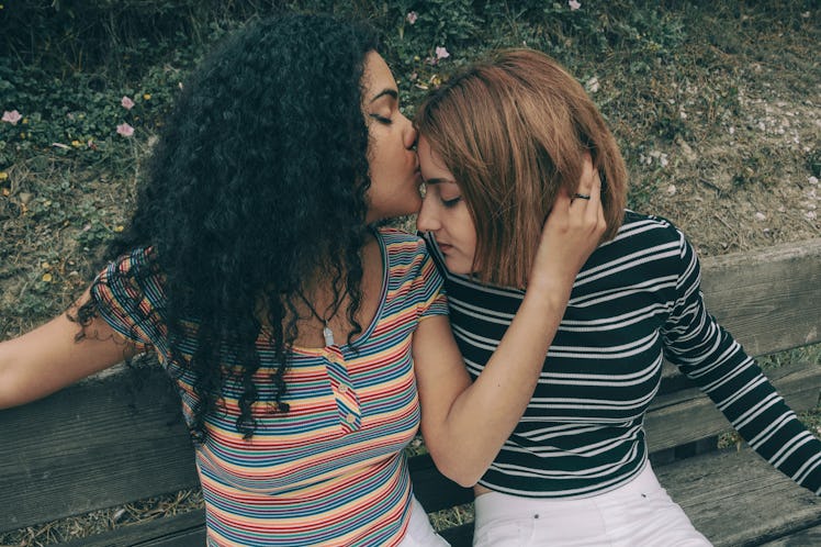 Two lesbian couple of different racial ethnic kissing on a bench
