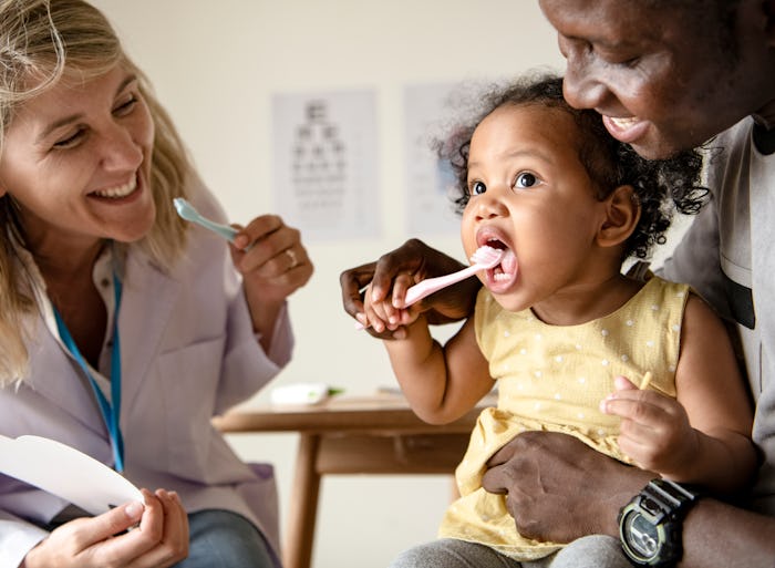 Dentist teaching a little girl how to brush her teeth